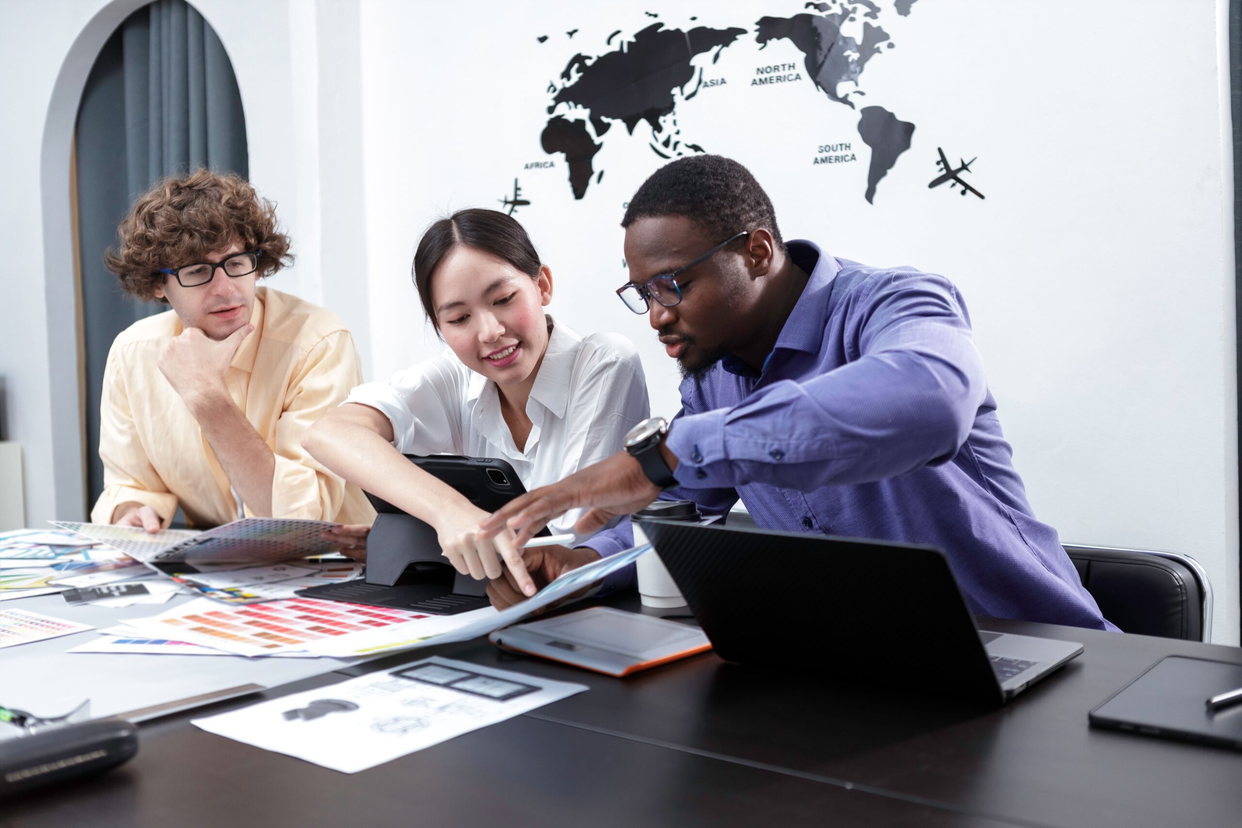 Three diverse marketing professionals collaborating on a content strategy at a modern office table with design materials and laptops.